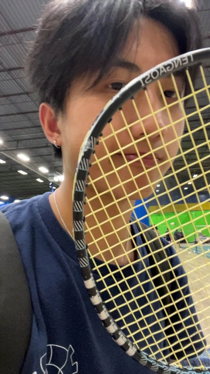 Chris holding a badminton racket close to the camera inside an indoor court