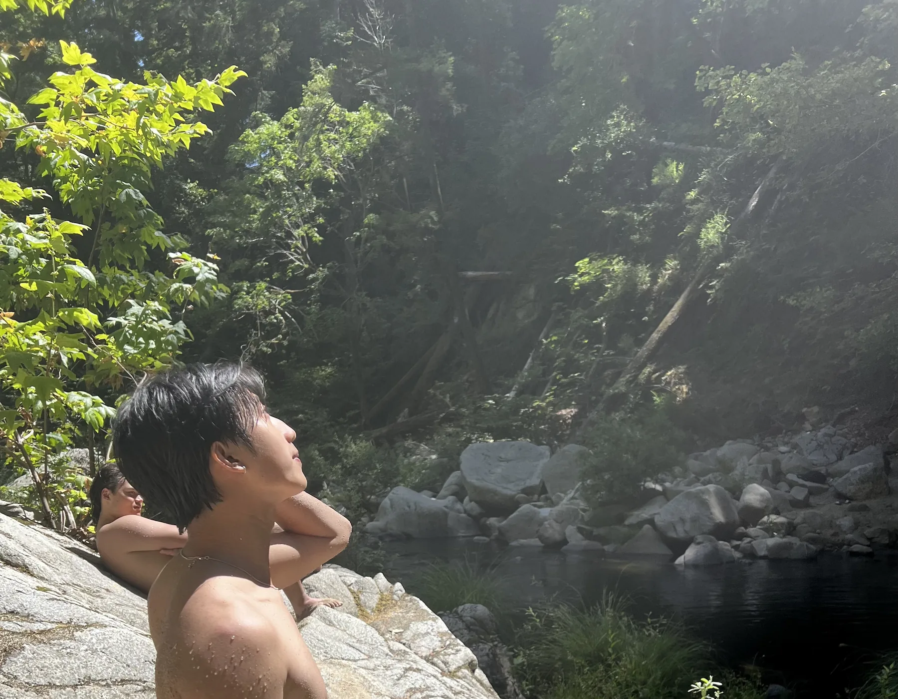 Chris sitting by a rocky swimming spot in the sun during an outdoor trip