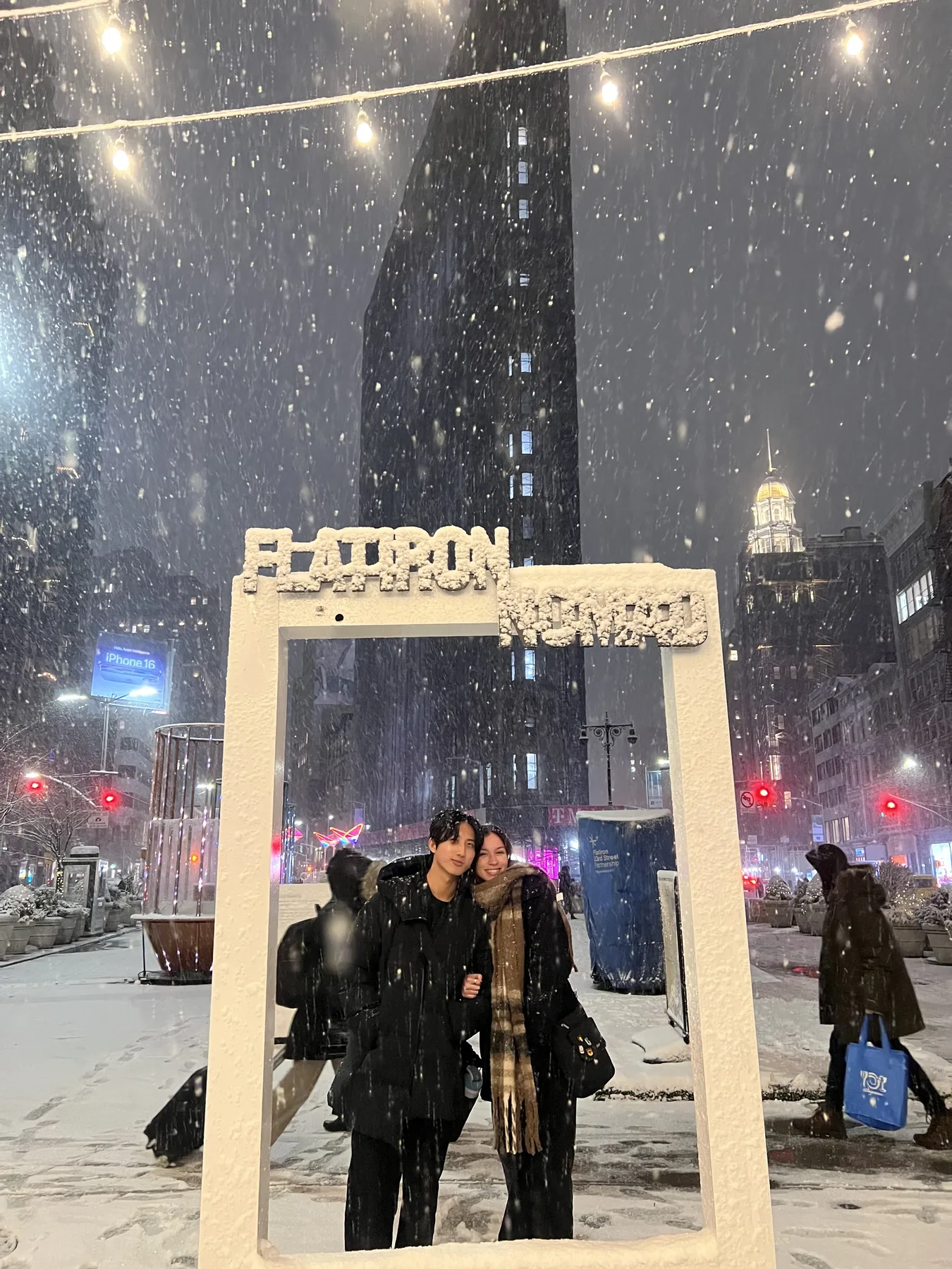 Chris and his partner posing together in heavy snow under a Flatiron Nomad frame in New York City