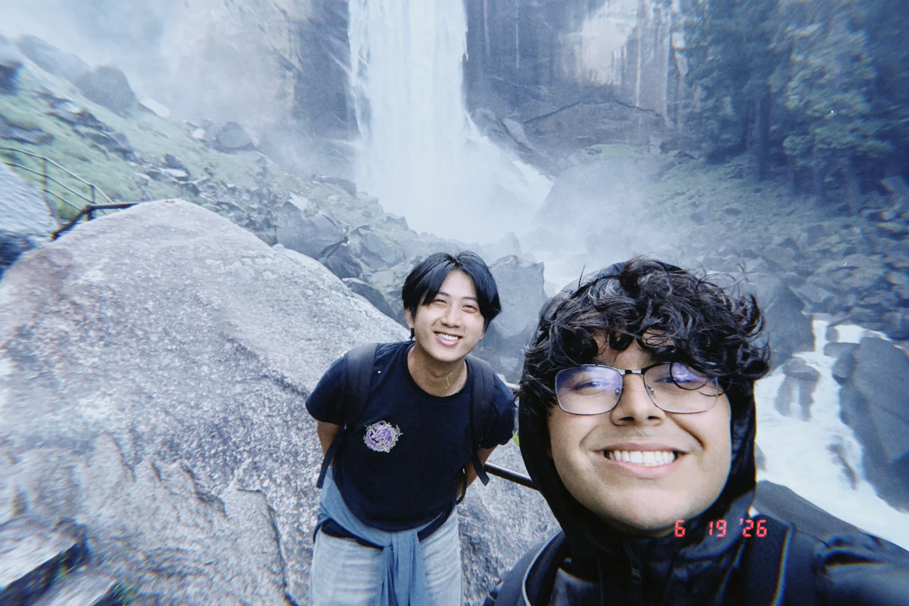 Chris and a friend smiling together in front of a large waterfall