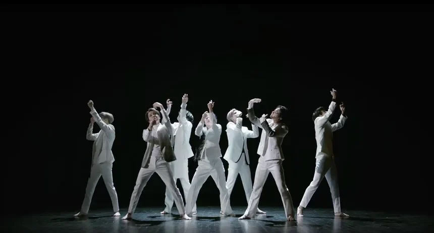 The seven members of BTS performing together in white suits on a dark stage